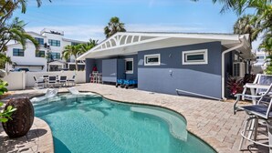 A swimming pool with a curved edge, surrounded by lounge chairs and a covered patio area. - Beach Home with Pool and Gas Grill! 2 min walk to Beach! (Holmes Beach)
