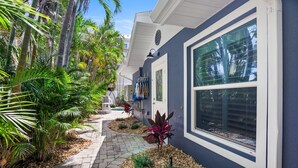 A pathway lined with tropical plants and a building with a large window. - Beach Home with Pool and Gas Grill! 2 min walk to Beach! (Holmes Beach)
