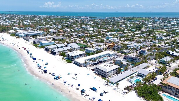 A coastal resort with beachfront villas, a swimming pool, and a beach with umbrellas. - Beach Home with Pool and Gas Grill! 2 min walk to Beach! (Holmes Beach)