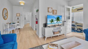 Una sala de estar moderna con televisor, mobiliario blanco y una obra de arte con motivos playeros.