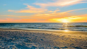 Une plage où l’on peut voir des empreintes de pas menant à l’eau, un ciel dégagé et le soleil se couchant à l’horizon.