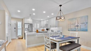 Une cuisine moderne avec des meubles blancs, un îlot central et un coin repas comprenant une table et des chaises.