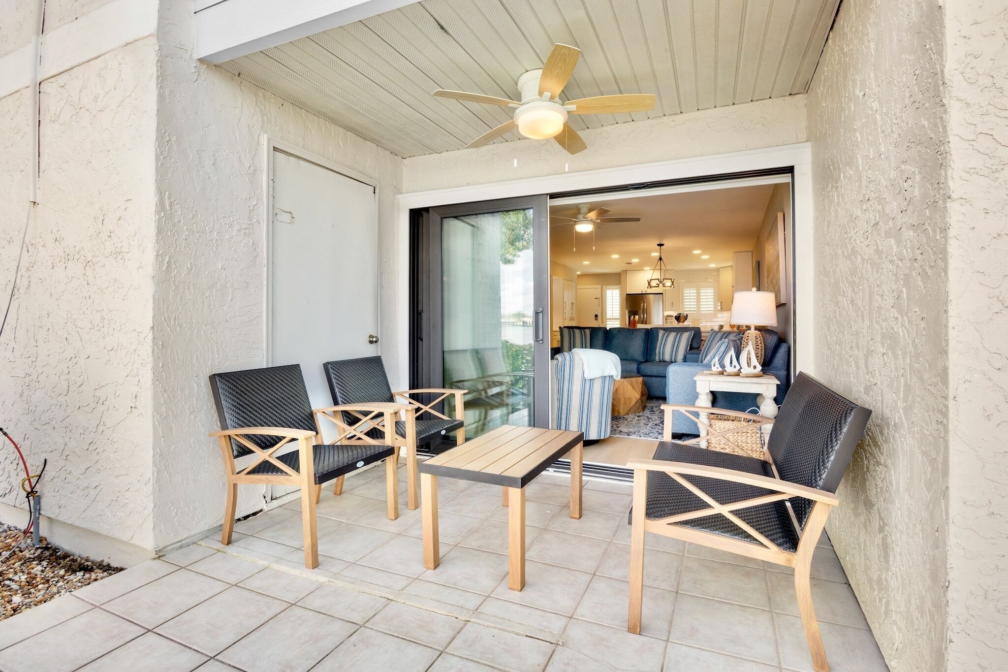 Une terrasse extérieure dotée de meubles en bois, d’un ventilateur de plafond et d’une porte-fenêtre coulissante donnant sur un espace de vie intérieur.