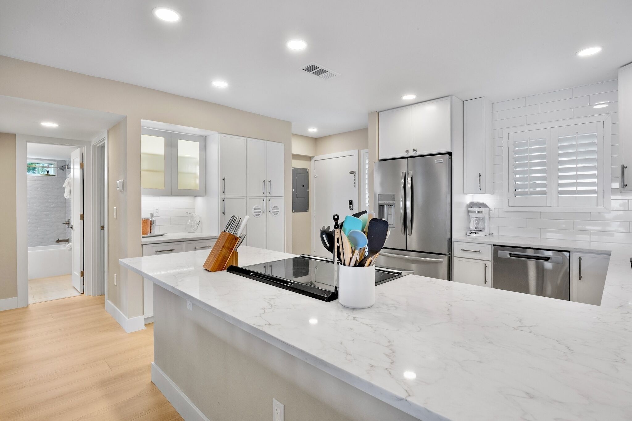 Una cocina moderna con gabinetes blancos, un refrigerador de acero inoxidable y una encimera de mármol.
