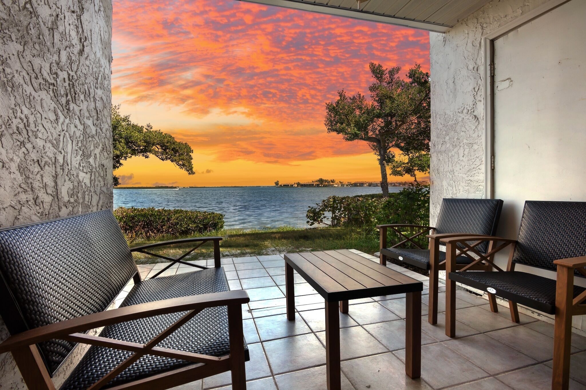 A patio with outdoor furniture, a view of the sea, and a sunset.