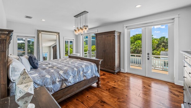 A bedroom with a large bed, wooden floor, and a view of the outdoors through large sliding glass doors. - North End Home, 5 Houses to Beach! Near Pine Ave! (Anna Maria)