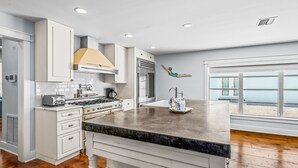 A modern kitchen with white cabinetry, a granite countertop, and a view of the beach through large windows. - North End Home, 5 Houses to Beach! Near Pine Ave! (Anna Maria)