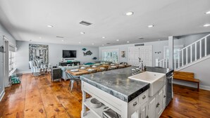 A spacious kitchen with a central island, wooden flooring, and a staircase leading to an upper level. - North End Home, 5 Houses to Beach! Near Pine Ave! (Anna Maria)