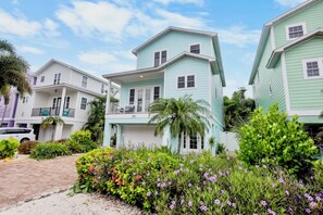 A row of two-story houses with balconies, surrounded by lush greenery and flowering plants.