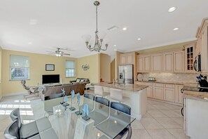 A modern kitchen with beige cabinets, a central island, and a dining area with a glass table and chairs. - Private Home with Pool, Near the Beach - Sand Dollar (Holmes Beach)