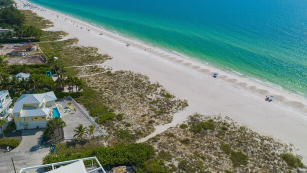 Une plage avec une longue étendue de sable, quelques parasols et un bâtiment doté d’une piscine.