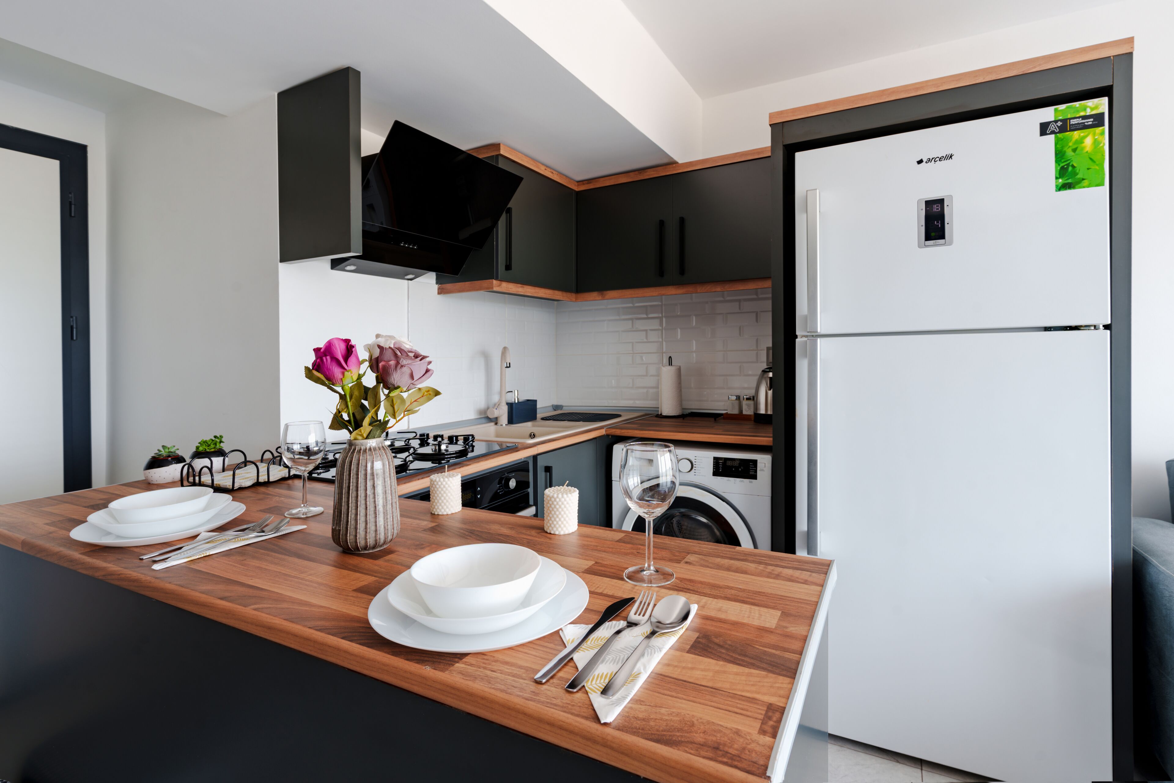 Una cucina moderna con piano di lavoro in legno, piano cottura integrato, lavatrice e frigorifero.