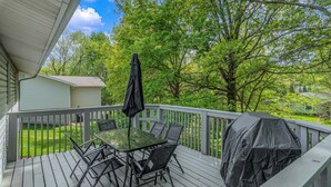 Una terraza techada al aire libre con una mesa, sillas, una parrilla y vistas a un paisaje verde.