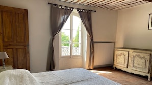 Un dormitorio con una cama, una puerta de madera, una ventana con cortinas, un radiador y un armario.