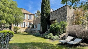 Una casa de piedra con césped cuidado, dos sillones de descanso y un muro de piedra.