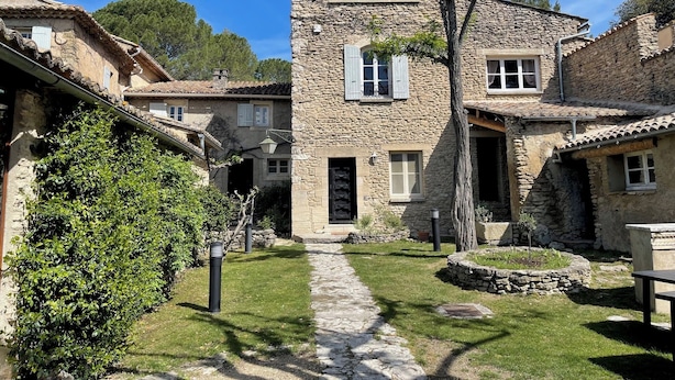 Un edificio de piedra con una entrada central, rodeado de un sendero de piedra y follaje.