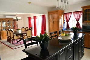 A modern kitchen with wooden cabinets, a central island, and a dining area with a red rug. - Upscale, Large country estate overlooking Spring Valley & the Caribbean Sea (Tower Isle)