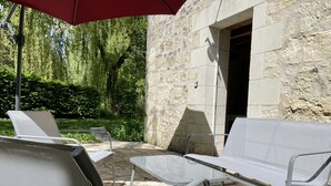 Un área de estar al aire libre con sillas de metal y una mesa, paredes de piedra y follaje al fondo.