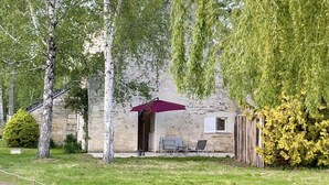Un edificio de piedra con un patio cubierto, mobiliario exterior y un jardín cercado.