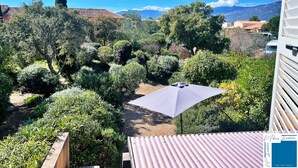 Ein Garten mit verschiedenen Sträuchern und einer Terrasse mit einem weißen Sonnenschirm.