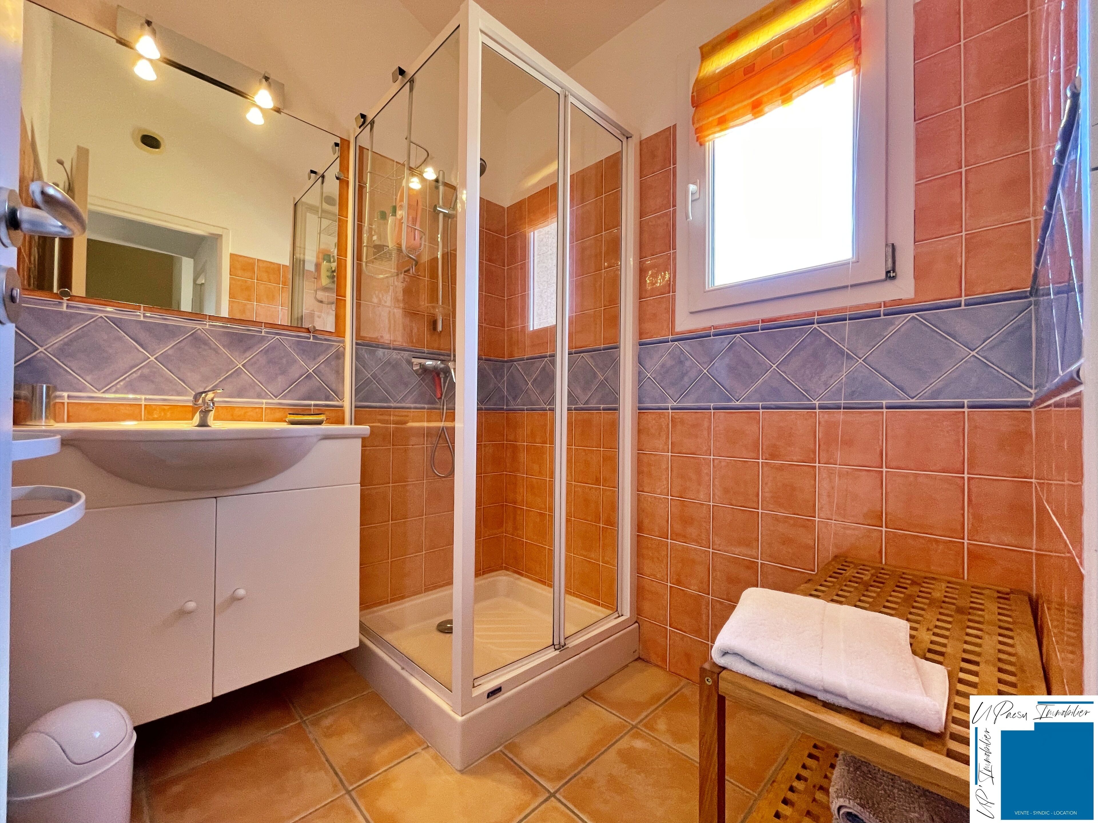 A bathroom with a glass-enclosed shower, a sink, and a wooden towel rack.