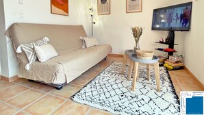 Ein Wohnzimmer mit einer Couch, einem kleinen Tisch mit einer Vase, einem Fernseher und Kunstwerken an den Wänden.