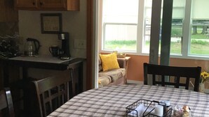 Un coin repas avec une nappe à carreaux, une machine à café et une fenêtre donnant sur un paysage verdoyant.