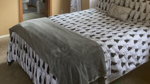 Une chambre à coucher comprenant un lit, un ventilateur de plafond, une fenêtre avec des rideaux et une porte donnant sur une salle de bain.
