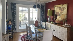 Un coin repas avec une table en verre, des chaises, un tapis à motifs et une vue sur une terrasse extérieure, accessible par une porte vitrée.