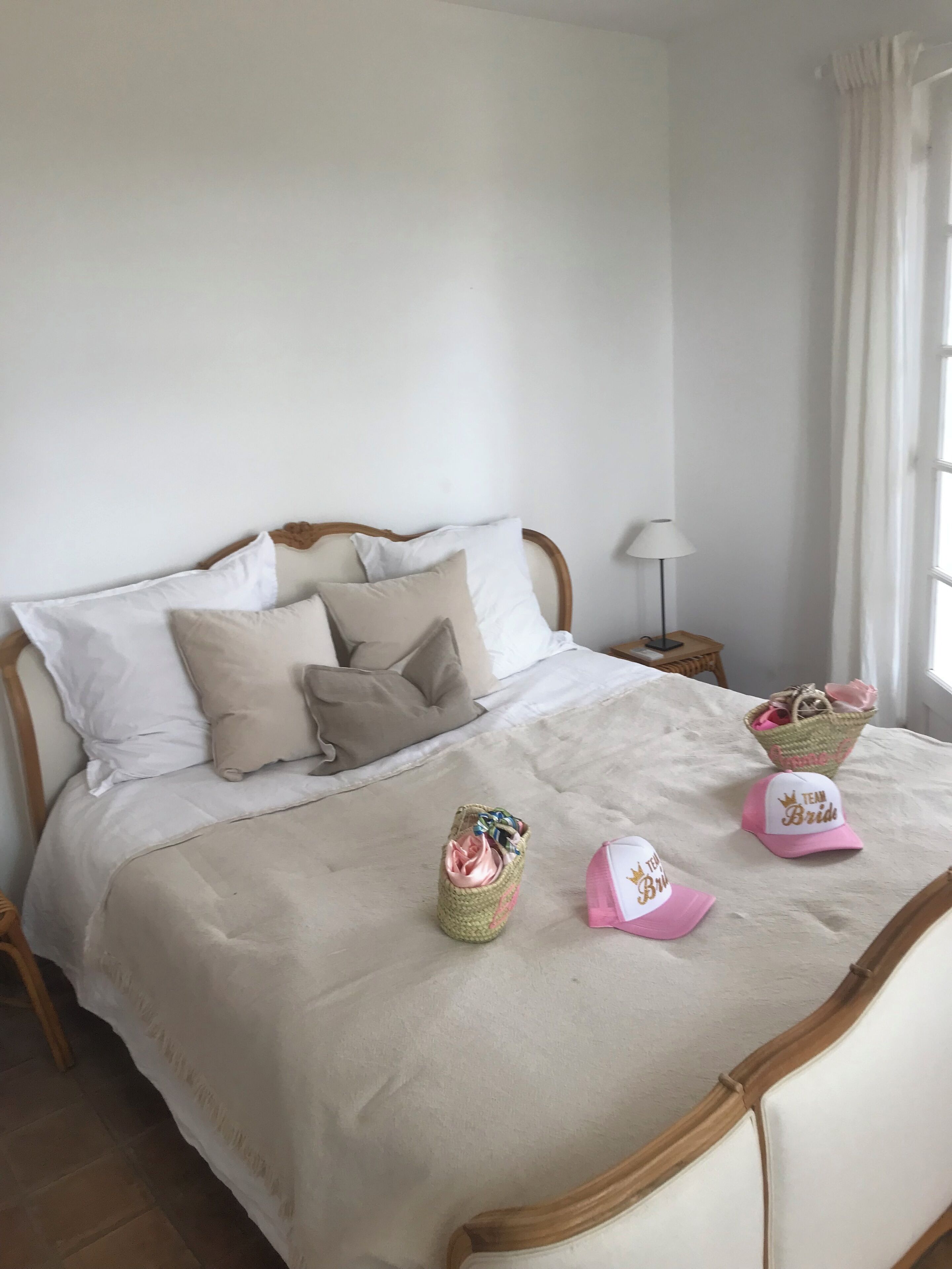 En pænt redt seng med et beige sengetæppe og puder, en natlampe og to kurve på sengen.