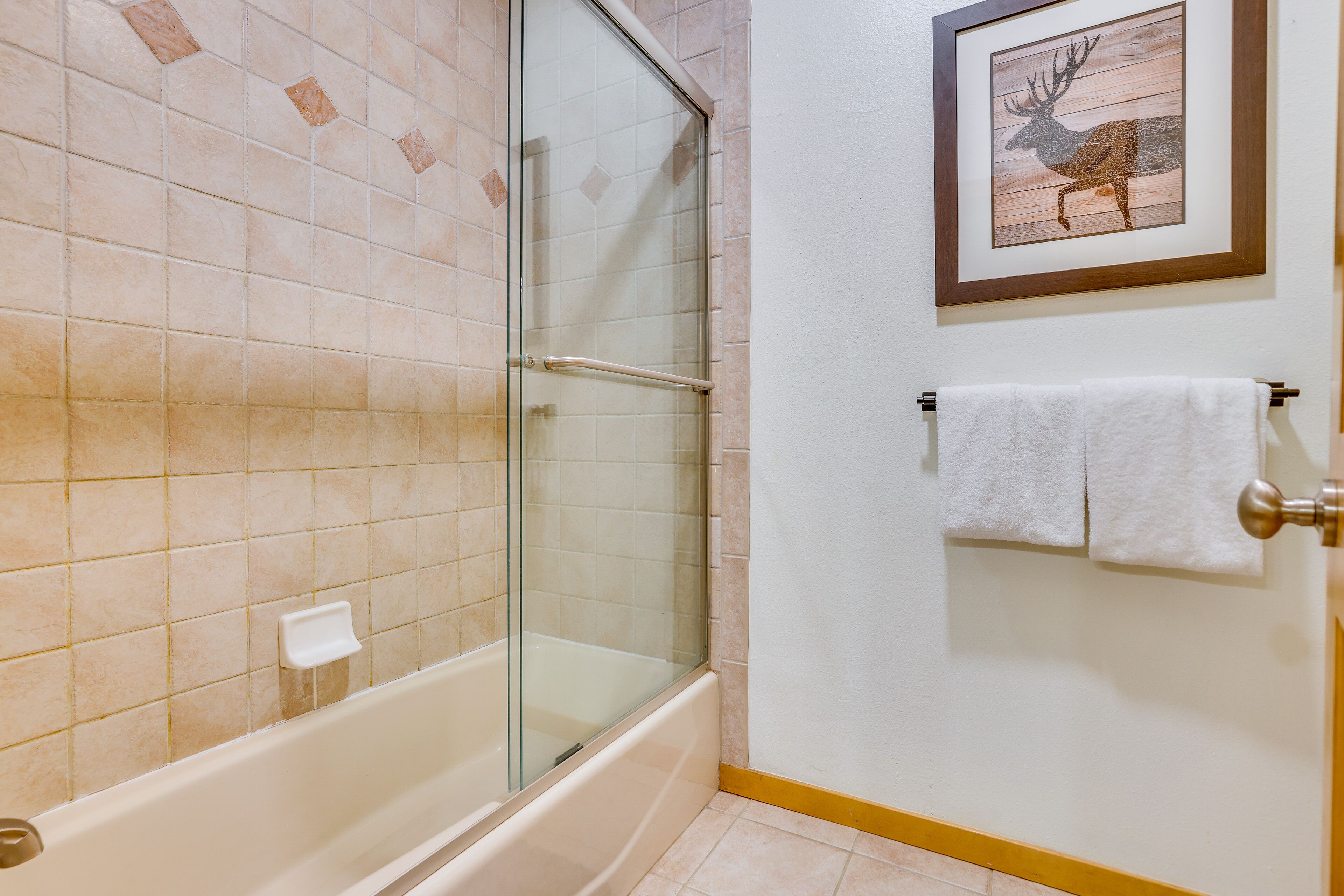 A bathroom with a glass-enclosed shower, a white bathtub, and a framed deer picture on the wall.