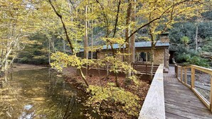 Eine Holzterrasse mit Blick auf einen ruhigen Fluss, umgeben von Bäumen im Herbstlaub.