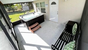 A covered outdoor area with a hot tub, a wooden bench, and a door. - Home near the Beach w/ Hot-tub and Movie Room (Fort Pierce)