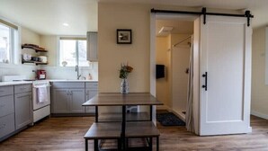 A modern kitchen with grey cabinets, a wooden table, and a sliding door leading to another room. - Greenough Loft (Missoula)