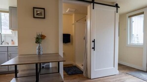 A room with a sliding door, a wooden table, a vase with flowers, and a view of a bathroom with a shower. - Greenough Loft (Missoula)