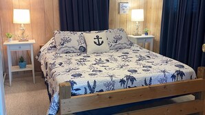 Un dormitorio con cama de madera, dos mesitas de noche con lámparas, ventilador de techo y decoración náutica.