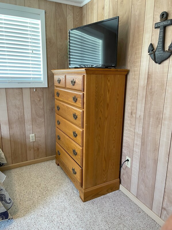 A wooden dresser with drawers, a television on top, a wall-mounted anchor decoration, and a window with blinds. - Bayfront Home w/Private Lighted Fishing Pier (Port Lavaca)