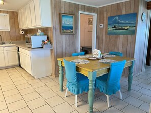 A dining area with a wooden table, blue chairs, and a painting of a boat on the wall.