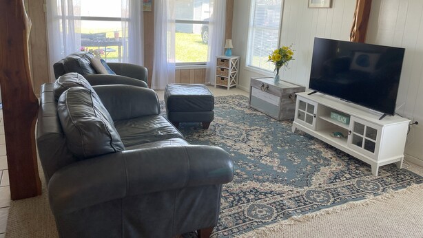 Una sala de estar con un sofá de cuero, un televisor de pantalla plana sobre un mueble blanco y una alfombra estampada.