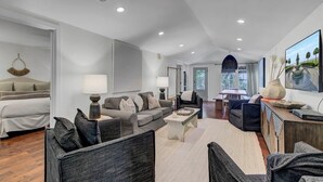 Un salon moderne avec un canapé, des fauteuils et une table basse. Il y a également un coin repas avec une table et des chaises. La pièce est dotée d'une grande fenêtre qui offre une vue sur l'extérieur.