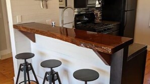 A modern kitchen with a wooden island, black bar stools, stainless steel appliances, and dark cabinetry. - Sugarloaf Golf Course View in the Heart of Leelanau County (Cedar)