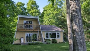A two-story house with a balcony, surrounded by lush greenery and a large tree. - Sugarloaf Golf Course View in the Heart of Leelanau County (Cedar)