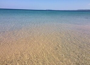 A beach with clear shallow water and a distant shoreline. - Sugarloaf Golf Course View in the Heart of Leelanau County (Cedar)