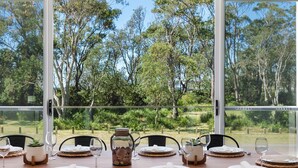 A dining table set for six with a view of a forest through large windows. - SeaSalt By The Sea Narrawallee (Narrawallee)