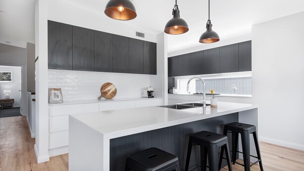 A modern kitchen with dark cabinetry, a white island, and black bar stools. - SeaSalt By The Sea Narrawallee (Narrawallee)