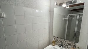 Een moderne badkamer met witte tegels, een houten wastafelmeubel, een spiegel en een douchecabine.