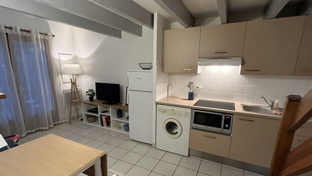 Een kleine keuken met een wasmachine, magnetron en een eethoekje met een tafel en stoelen.