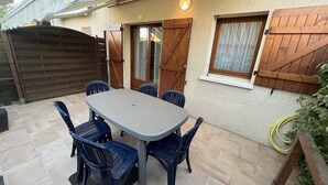 Een terras met een tafel en stoelen, een houten poort en een raam met luiken.