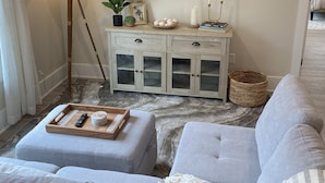 Un soggiorno con una TV a schermo piatto montata a parete, una lampada da terra, un tavolino con oggetti decorativi e un divano grigio.