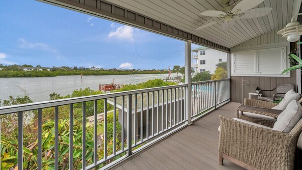 A covered balcony with wicker furniture, a ceiling fan, and a view of a river and buildings.